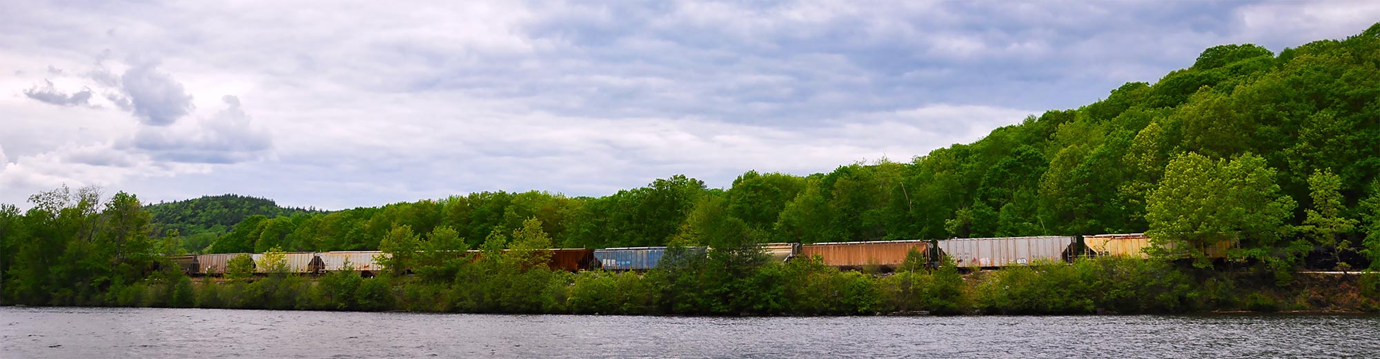 A freight train rolls alongside a river bank